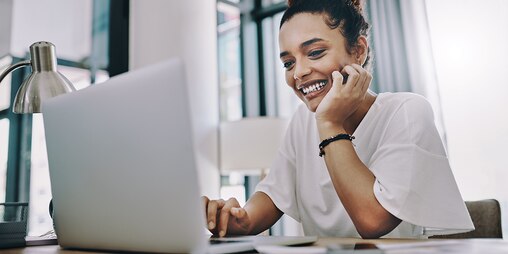 Woman sat at desk looking at laptop and smiling