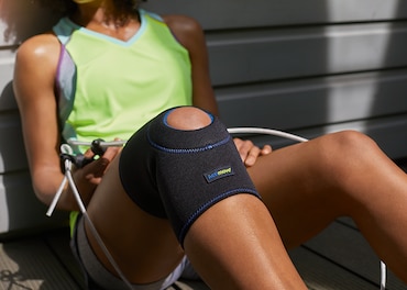 Woman wearing sports clothes and a knee support rests against a wall - close up