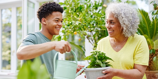 Grandson watering the plant his grandma is holding with a watering can