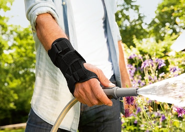 Man uses a hose to water the garden while wearing a wrist support 