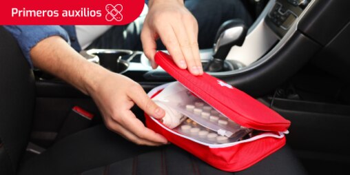 Persona abriendo el botiquín de primeros auxilios para el coche, mostrando medicamentos y gasas en su interior. Se lee “Primeros auxilios” en un recuadro.