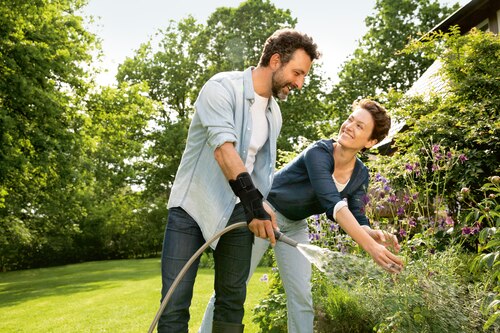 Men gardening together with partner, wearing an Actimove Professional Line Manus Forte Wrist Brace while watering plants with hose
