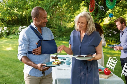 Man interacting with hostess at garden party, wearing an Actimove Professional Line Umerus Comfort Shoulder Immobilizer
