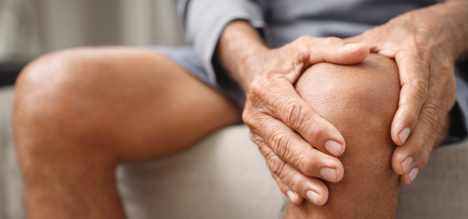 Hombre con las manos sobre la rodilla debido a un brote de artritis reumatoide que le causa dolor.