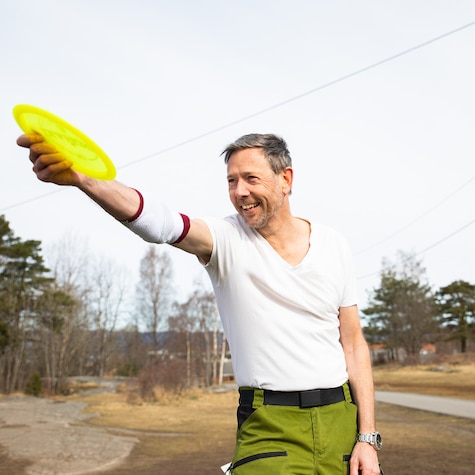 Man har en støtte rundt armen og kaster en frisbee. Man har en støtte rundt armen og kaster en frisbee.
