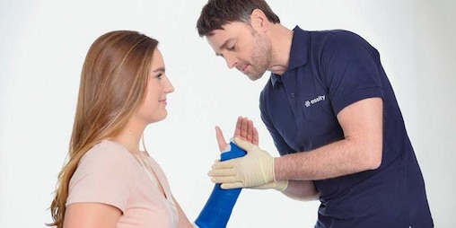 A male doctor or nurse checks arm cast of a woman, gently touching her arm in a medical treatment setting.