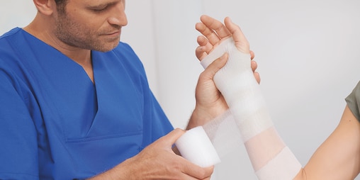Male nurse in blue scrubs gently applying a bandage to a woman's arm in a medical treatment scenario.