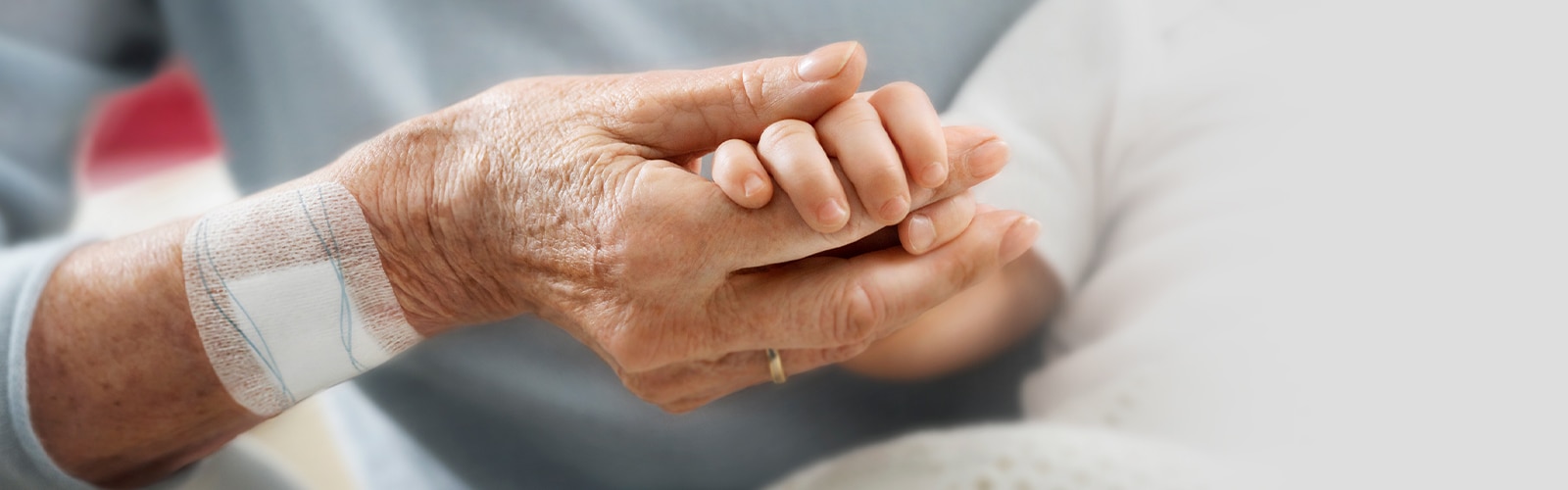 Een oudere vrouw met een wondpleister op haar rechterarm houdt de hand van een baby vast.  