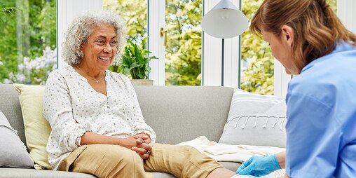 A patient smiles as a healthcare professional applies a Cutimed Sorbact dressing in a home setting.