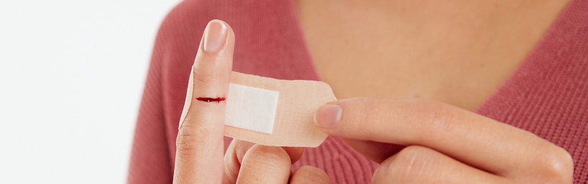 Kvinne som behandler et kutt i fingeren sin med en Leukoplast elastic plaster.
