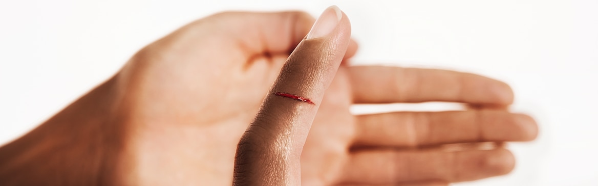 Woman treating her cut finger with a Leukoplast elastic finger dressing.