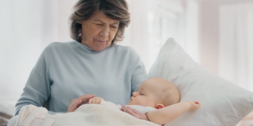 Elderly woman holding a sleeping baby with Leukomed skin sensitive plaster on the right arm.
