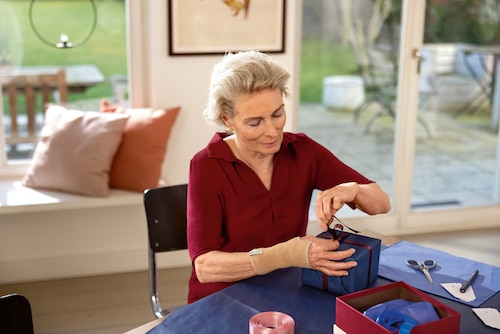 Woman wearing Actimove wrist support for arthritis, looking comfortable bending her wrist wrapping gifts