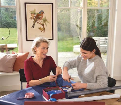 Happy woman wearing Actimove wrist support for arthritis, with granddaughter, looking comfortable bending her wrist wrapping gifts