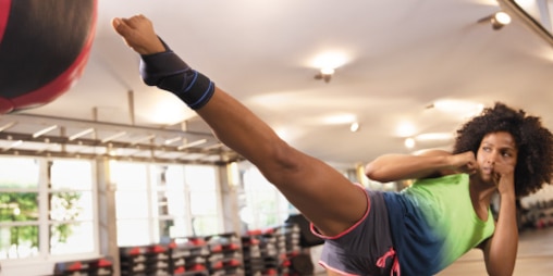 Kobieta kopiąca piłkę na siłowni podczas treningu z ortezą stawu skokowego Actimove Sports Edition z krzyżującymi się paskami