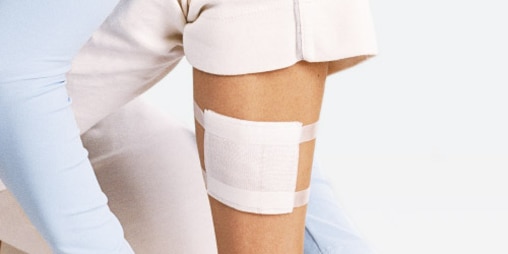 Una coscia, parzialmente coperta da pantaloncini bianchi, con applicata una medicazione. 