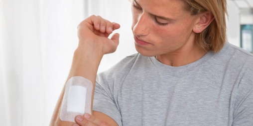 Young man looking at his right forearm, on which a large wound dressing is affixed.