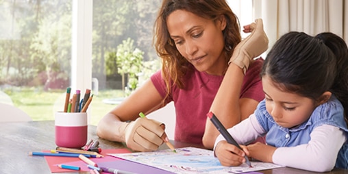 Matka z córką siedzą przy stole, kolorując rysunek