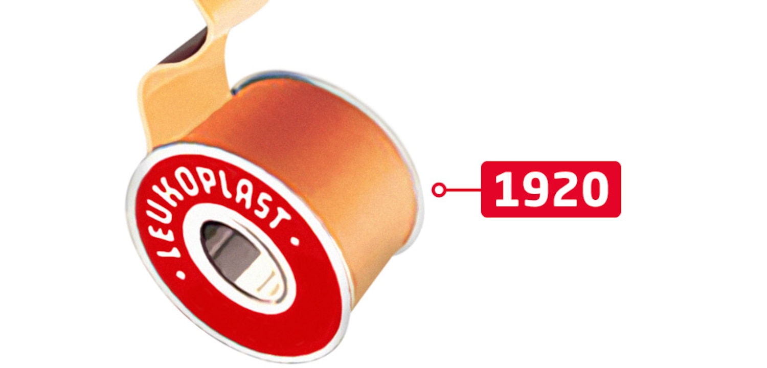 Naast de datum 1920 zien we een bovenaanzicht van de iconische rode Leukoplast-tape met zelfklevende hechtpleister.