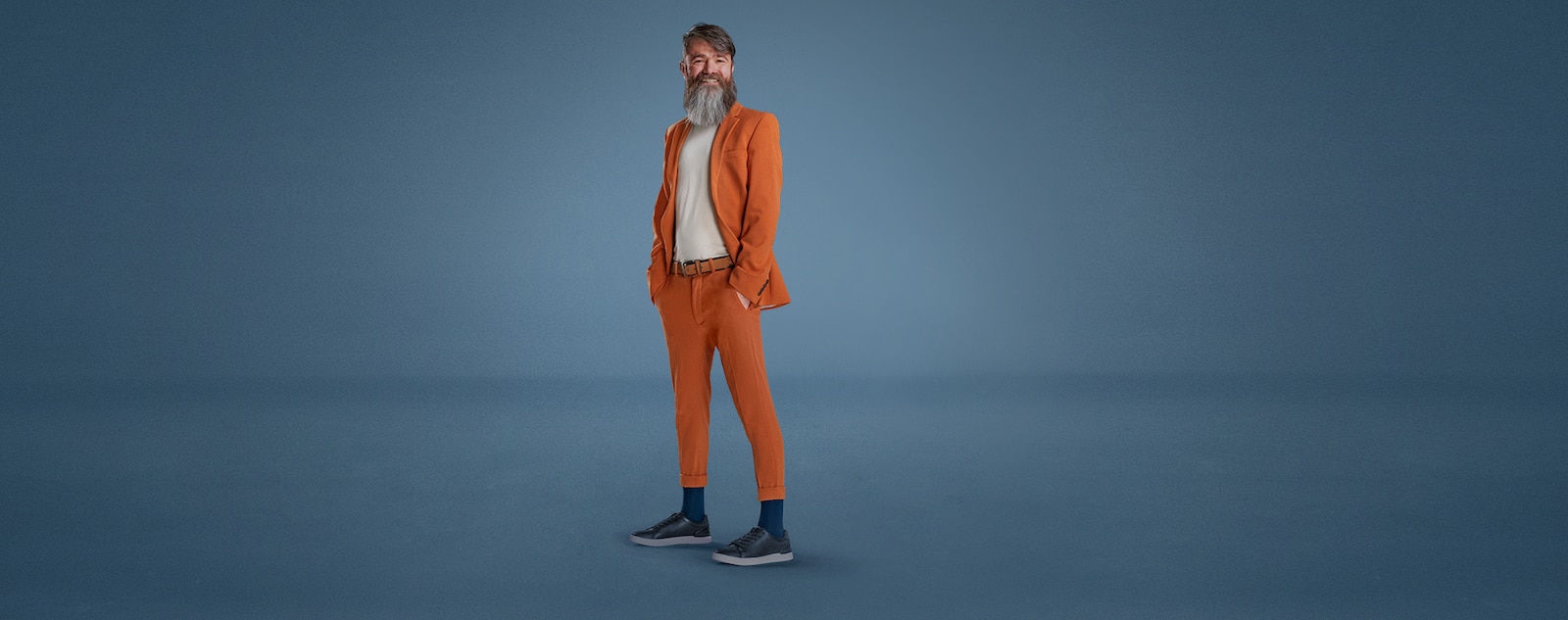 A man with a long beard stands wearing an orange suit and a pair of blue JOBST forMen socks