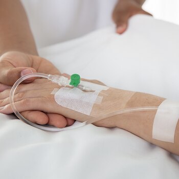 Sygeplejerske, der holder en patients hånd, med nærbillede af Leukomed I.V. film fra Leukoplast