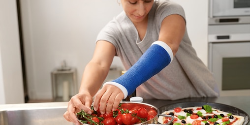 A woman wearing an arm cast preparing food in a kitchen.