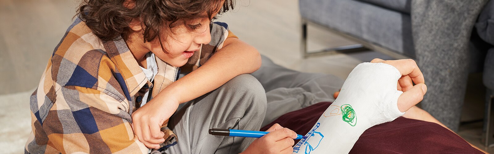 A young boy drawing on someone's arm cast with coloring pens.