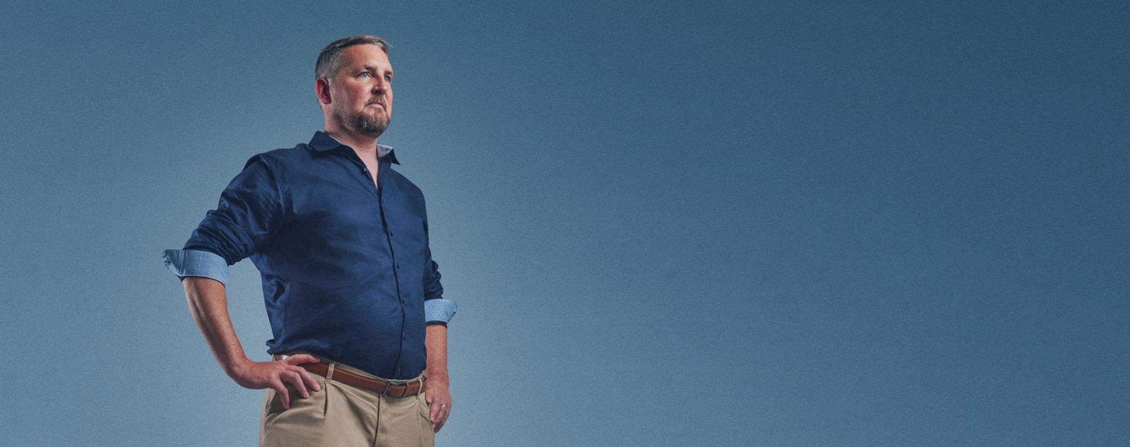 Gary står självsäkert med händerna på höfterna, klädd i en blå skjorta.