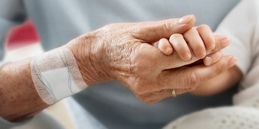 Een oudere vrouw met een pleister op haar rechterarm houdt de hand van een baby vast. 