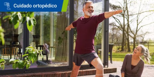 Hombre sonriente con ropa deportiva y un soporte para las rodillas hace ejercicios de estiramiento al aire libre mientras una mujer mira 
