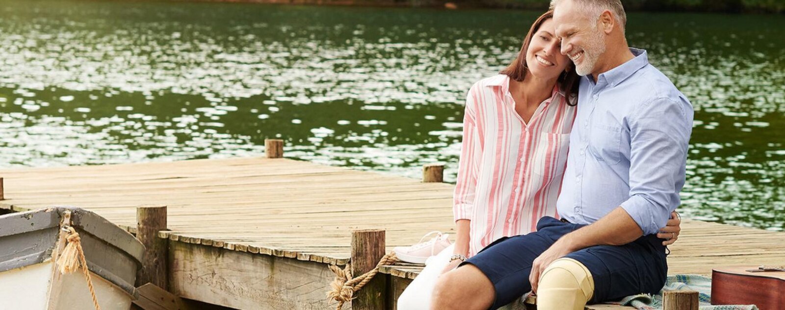 A woman and man are sitting by a lake holding each other and looking at the water