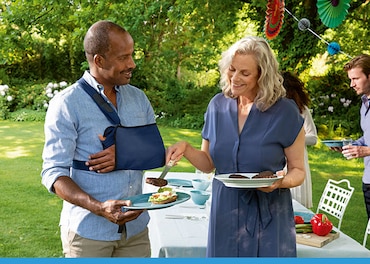 Man wearing a shoulder immobiliser holding a plate at a BBQ