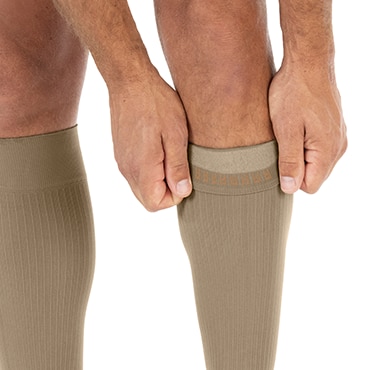 JOBST forMen beige color socks are being pulled up on the calf, showing SoftFit band which helps sock stay in place JOBST forMen beige color socks are being pulled up on the calf, showing SoftFit band which helps sock stay in place
