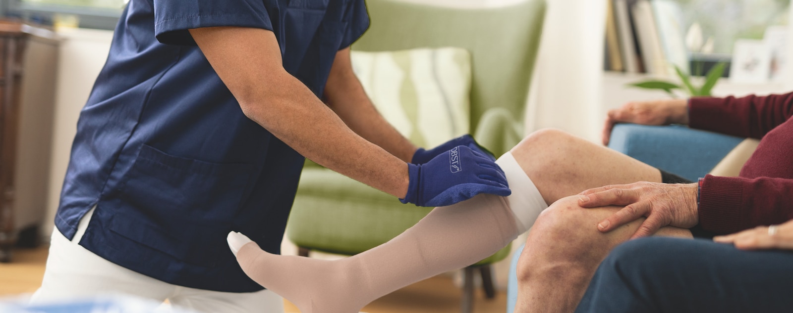 Healthcare professional adjusting compression stocking on a patient's leg while seated.