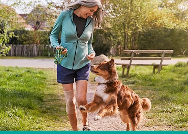 Una donna con fastidi al ginocchio indossa una ginocchiera Actimove per passeggiare tranquillamente con il suo cane.