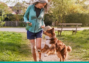Kobieta nosząca opaskę na kolano i ubrana w codzienny strój na spacerze z psem spuszczonym ze smyczy