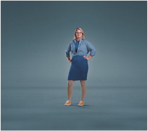 A woman wearing glasses standing against a plain blue background with both hands on her hips, dressed in a blue shirt, blue skirt, orange shoes, and JOBST Relief compression stockings.