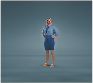 A woman standing against a plain blue background with both hands on her hips, dressed in a blue shirt, blue skirt, and orange shoes, wearing JOBST Relief compression stockings.