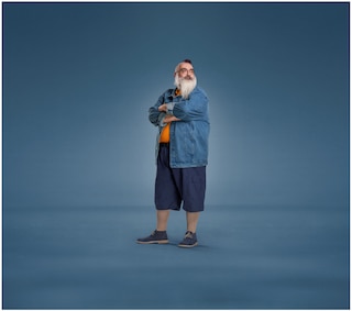 A bearded man with crossed arms, dressed in a denim jacket, orange shirt, navy shorts, and sneakers, wearing JOBST UlcerCare compression socks.