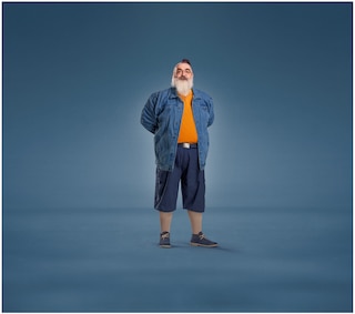 A bearded man wearing a denim jacket, orange shirt, navy shorts, and sneakers, paired with JOBST UlcerCare compression socks.