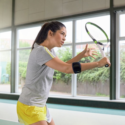 Una donna con una gomitiera mentre solleva in aria una racchetta da tennis Una donna con una gomitiera mentre solleva in aria una racchetta da tennis