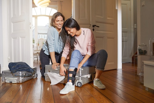 Woman at home packing for a trip together with girlfriend, wearing an Actimove Professional Line TaloCast Ankle Brace
