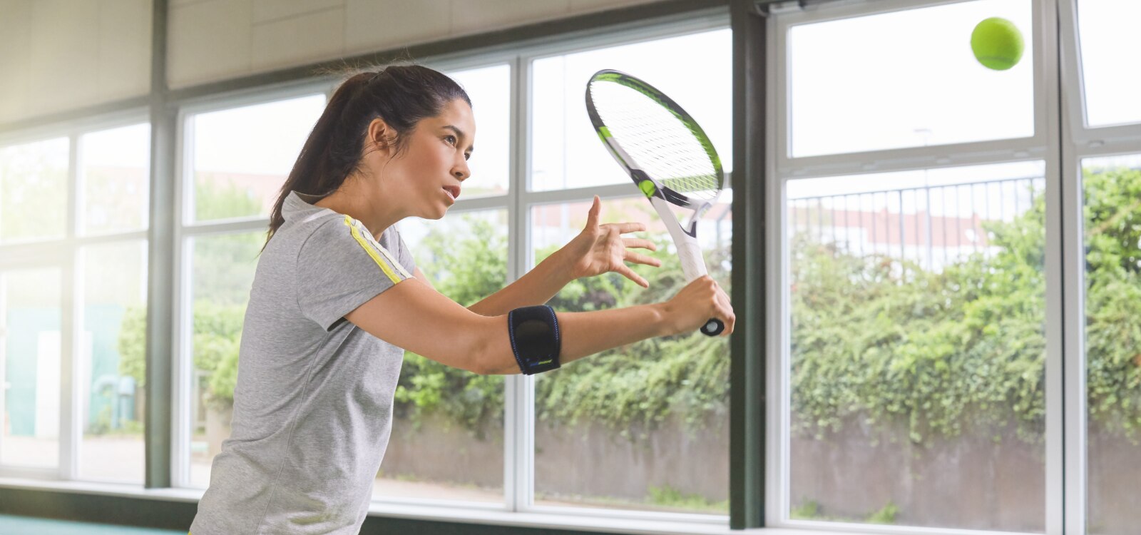 Mujer jugando al tenis mientras usa la codera deportiva Actimove Sports Edition para la epicondilitis.