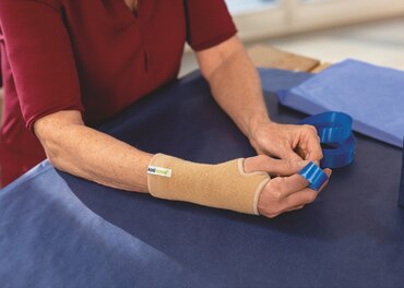 Ældre kvinde med håndledsbandage binder sløjfer, mens hun sidder ved et bord.