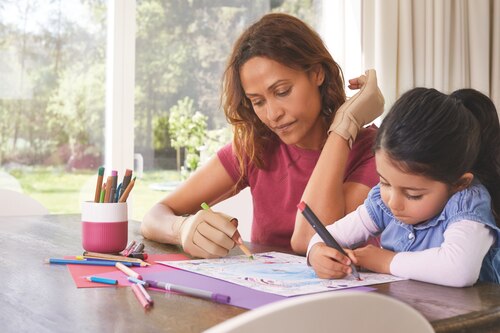 Woman wearing Actimove arthritis gloves, sitting at the desk with her daughter
