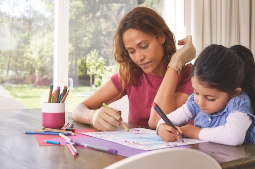 Woman wearing Actimove arthritis gloves, sitting at the desk with her daughter
