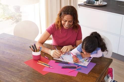 Happy woman wearing Actimove arthritis gloves support for arthritis, sitting at the desk with her daughter, drawing

