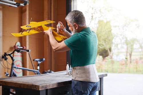 Man in his workshop building a plane model, wearing an Everyday Supports Back Support with High Density Panel
