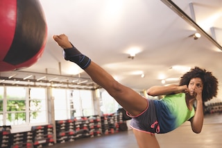 Egy nő edzés közben éppen egy labdába rúg az edzőteremben, és Actimove Sport bokastabilizátort visel

