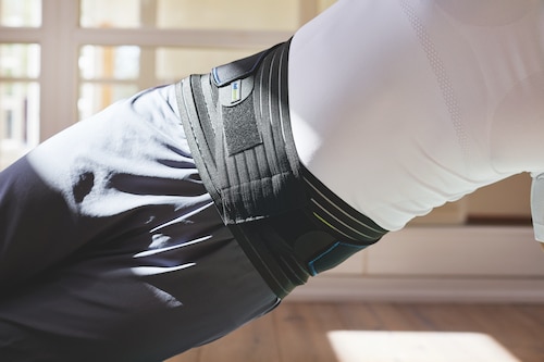 Front view of man at gym performing side plank exercise, wearing an Actimove Sports Edition Back Support with 4 Stays
